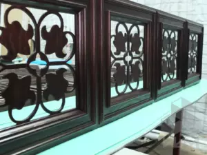 Вид секции декоративной световой стеновой панели для ресторана из фанерованного МДФ и массива дуба с прорезанным сквозь орнаментом, покрытой затемняющим лаком, в цеху.
